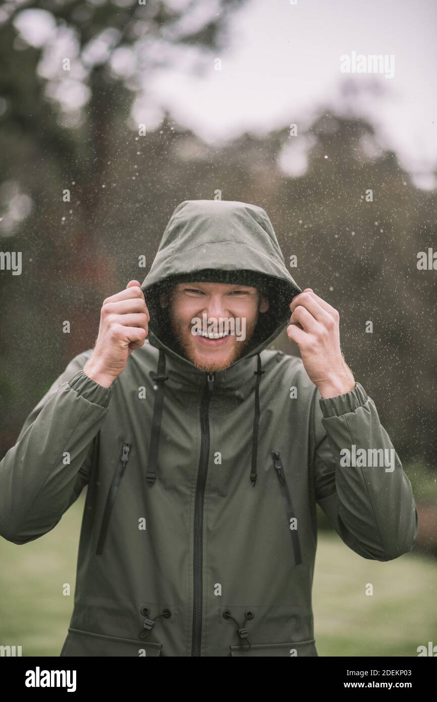 Young man in a green coat walking in the rain and smiling Stock Photo ...