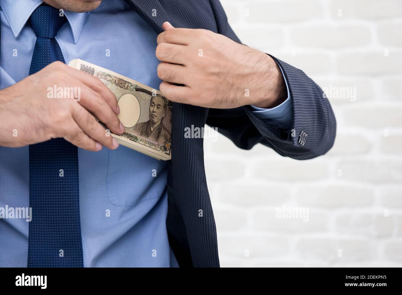 Businessman putting money, Japanese yen banknotes, into his suit pocket - corruption concept Stock Photo