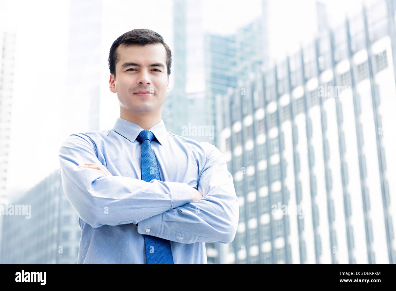Handsome young businessman leader confidently standing with arm crossed in city office building background Stock Photo