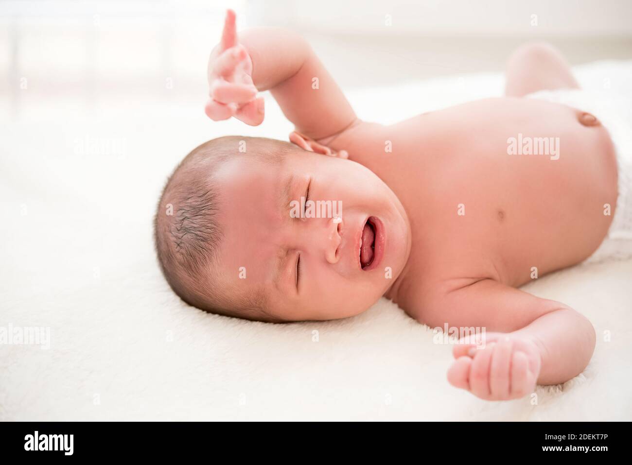 Unhappy shirtless newborn baby lying and crying on the