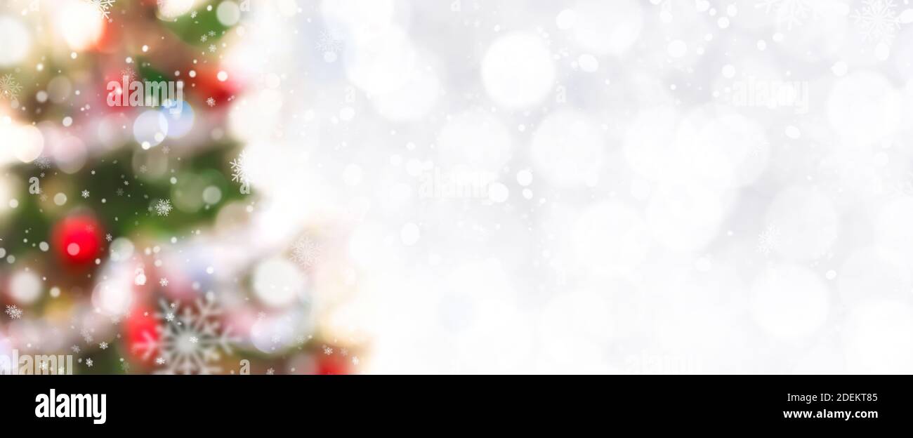 Abstract white bokeh with snow and blurred decorated Christmas tree at border - panoramic banner background, festive theme Stock Photo