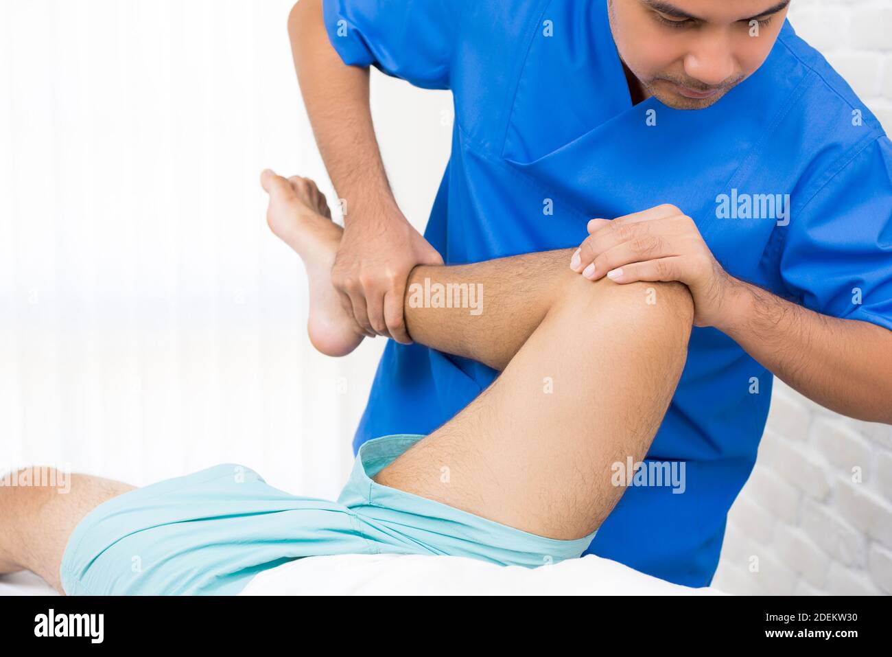 Doctor (therapist) holding leg of male patient stretching his lower back while lying on the bed in hospital - physiotherapy concept Stock Photo