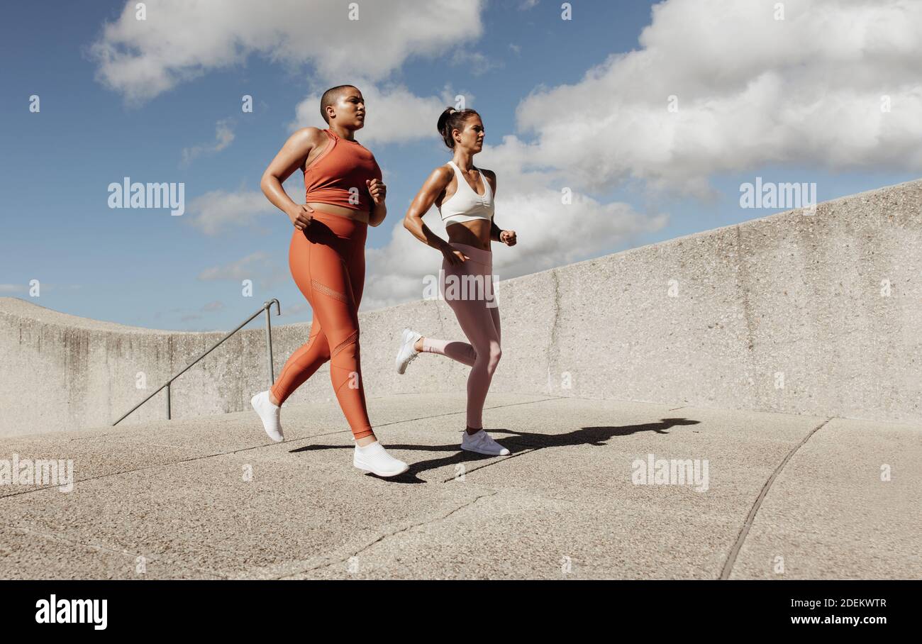 Two women jogging together. Female friends in sports wear running in morning. Stock Photo