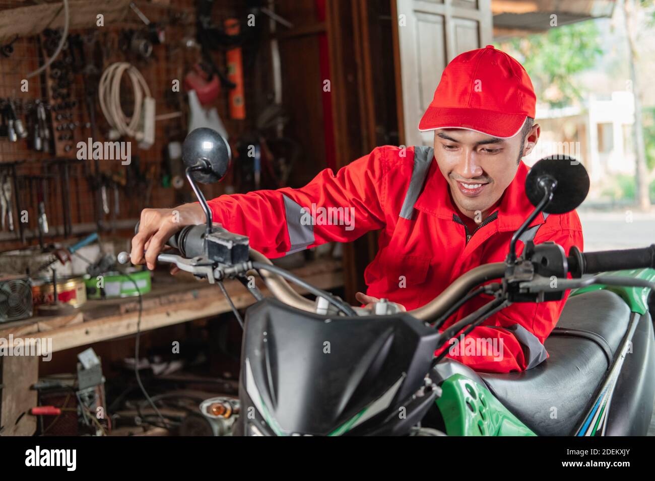 mechanic in a wearpack checks the engine throttle of the dirt bike in the garage Stock Photo