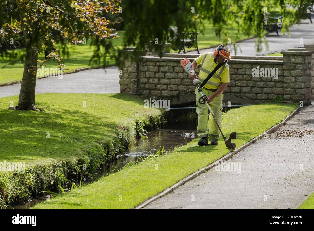 A Cormac worker strimming grass in Trenance gardens in Newquay in Cornwall. Stock Photo