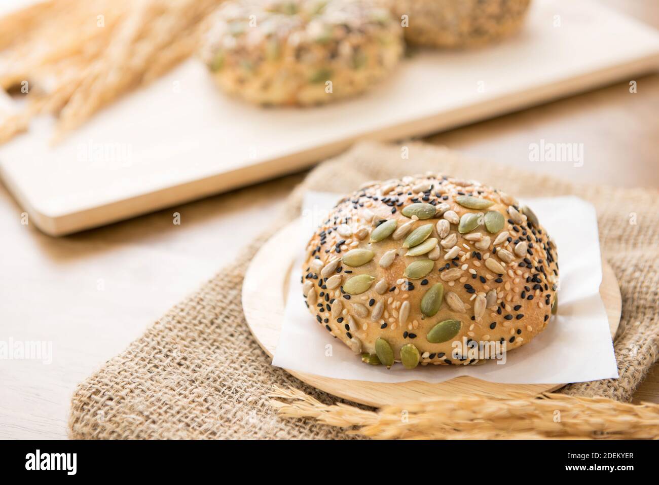 A healthy oven baked multigrain bread bun served on a wooden plate in a bakery Stock Photo