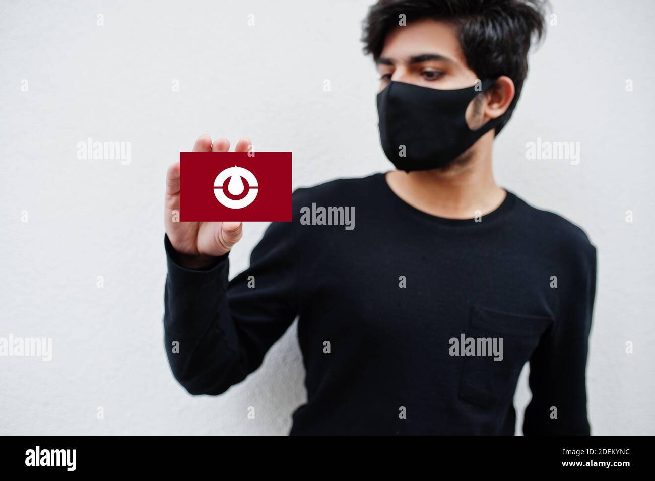 Japanese man wear all black with face mask hold Kochi flag in hand isolated on white background. Prefectures of Japan сoronavirus concept. Stock Photo