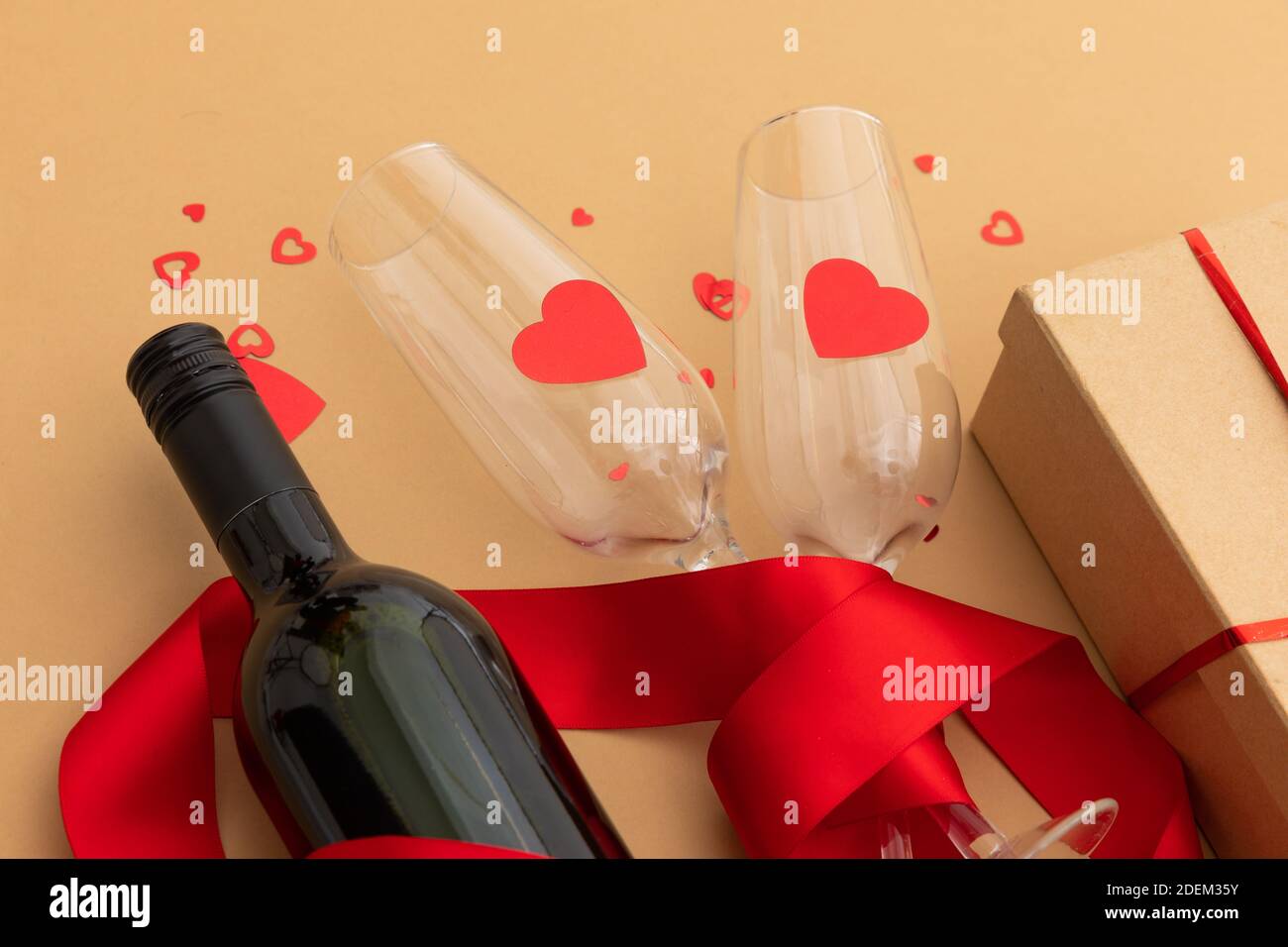 Bottle of wine, glasses with red hearts and present on brown background Stock Photo