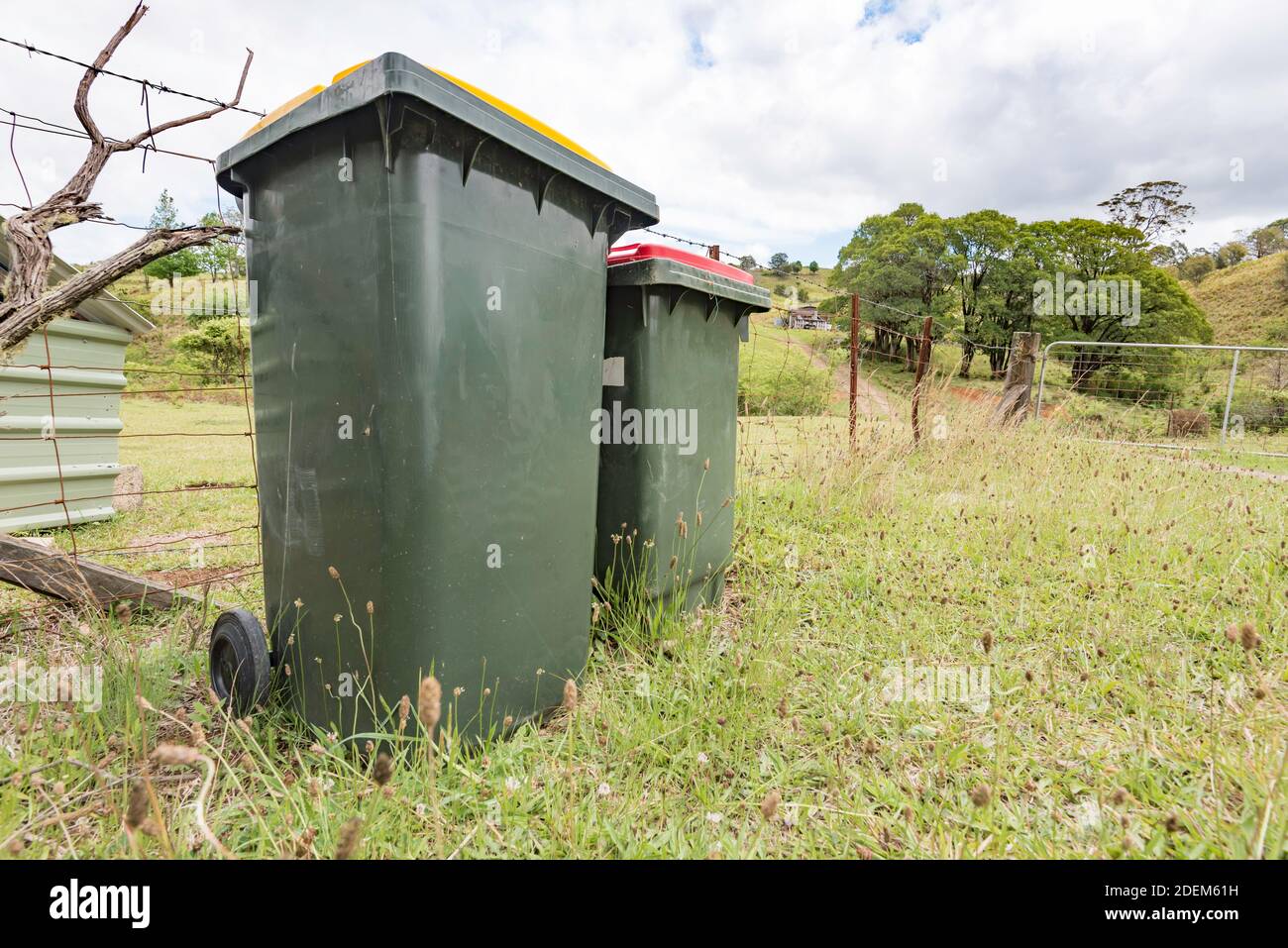 A domestic waste and recycling bin sit at a fence on a grassy verge outside a farm in New South Wales, Australia Stock Photo