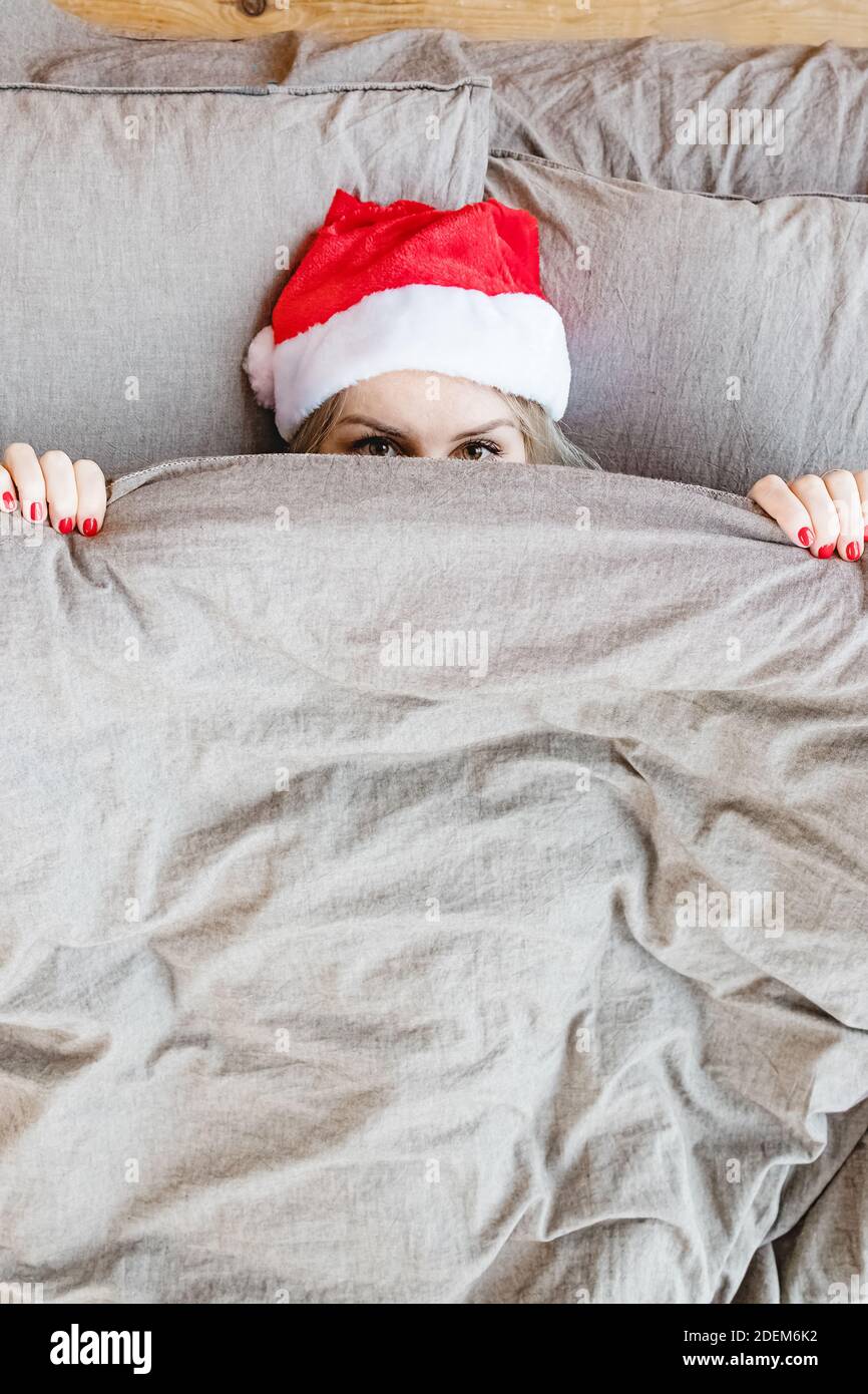 Woman in bed wear santa red hat covering her face with blanke Stock Photo