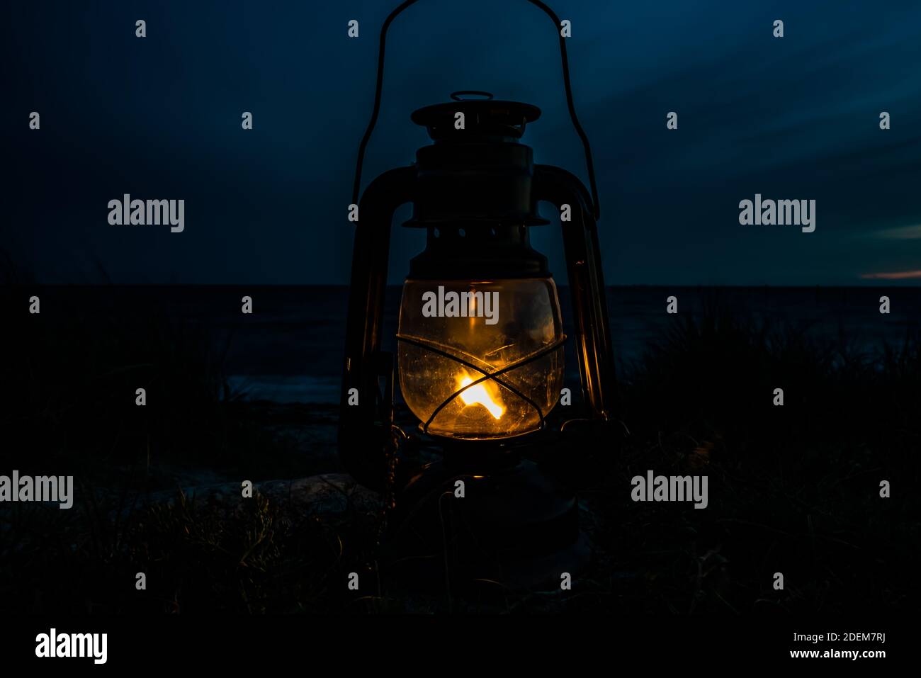 Old classic oil lantern burning with an orange flame by the ocean at dusk. . High quality photo