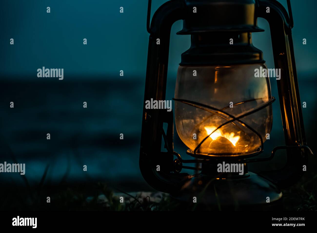 Old classic oil lantern burning with an orange flame by the ocean at dusk. . High quality photo Stock Photo