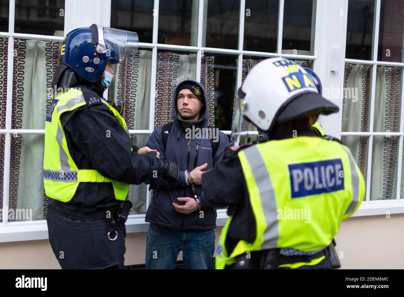 Anti-lockdown protest, London, 28 November 2020. An arrested protester in handcuffs stands with police officers in riot helmets. Stock Photo