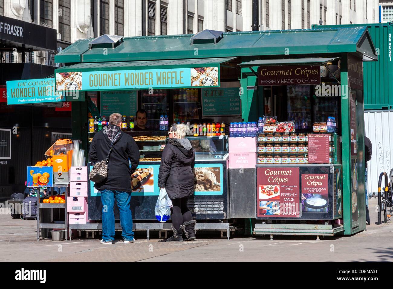 London, UK, April 1, 2012 : Tourist buying a Belgian waffle at a restaurant food street market stall also selling gourmet crepes and refreshments in t Stock Photo