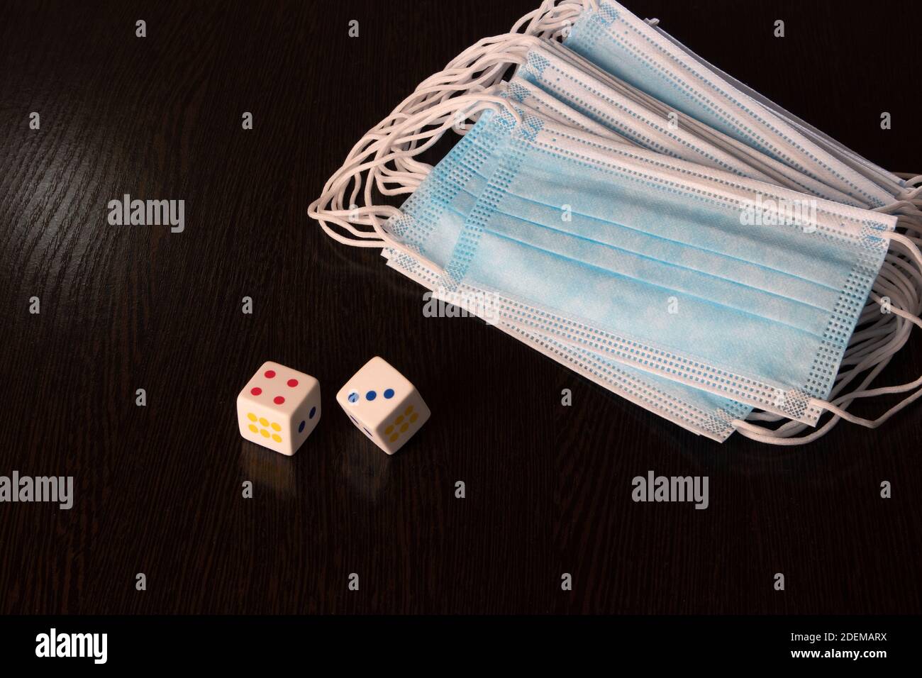 Pack of medical protective face masks and two dices lying on a dark wooden surface Stock Photo