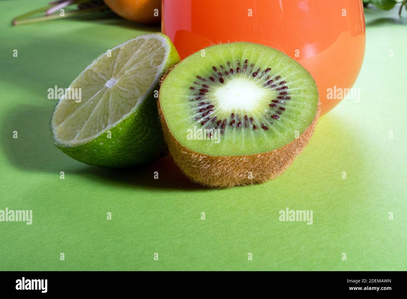 Composition of glasses with orange juice, lime, kiwi and verdure on a light green background Stock Photo
