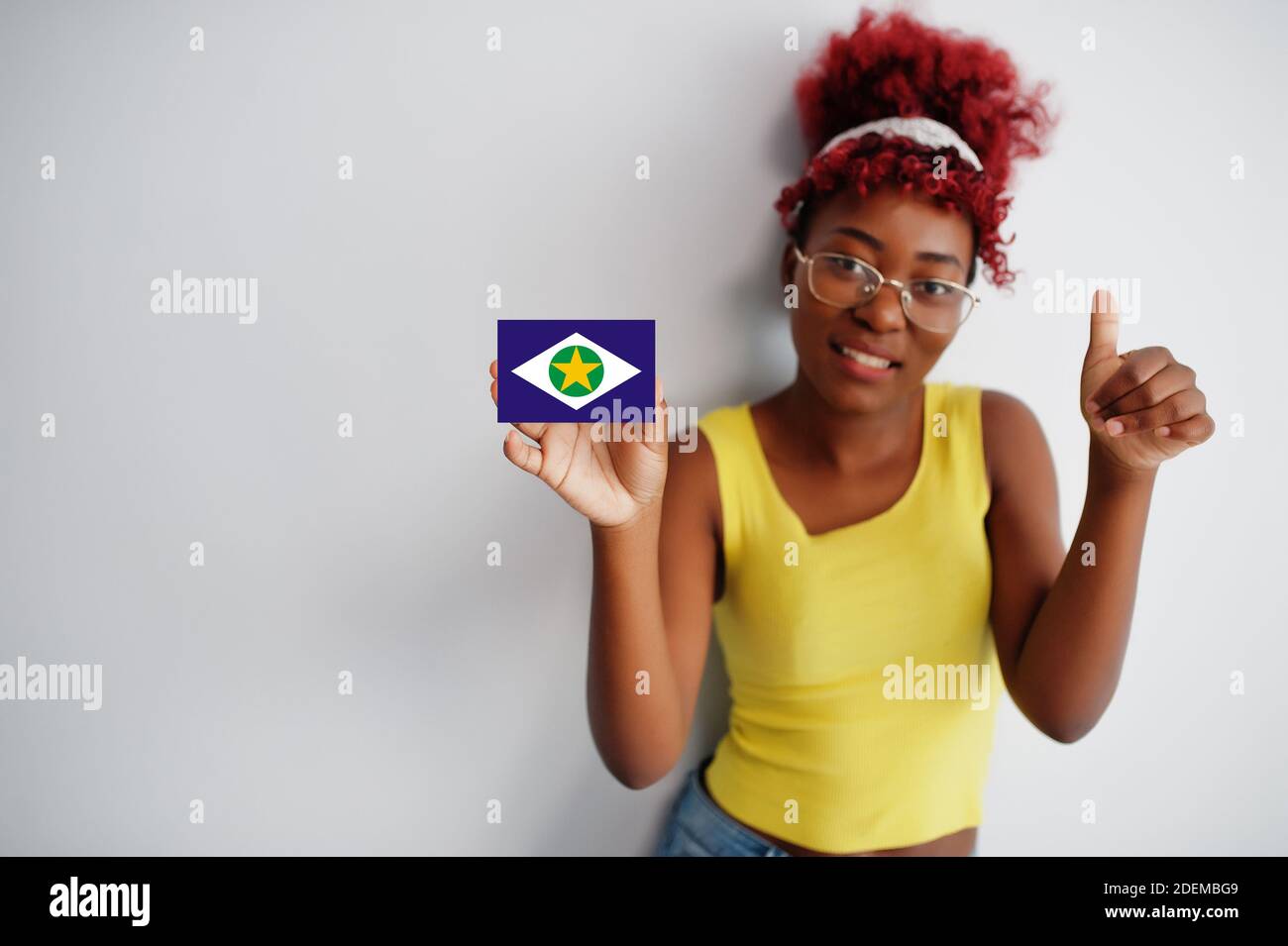 Brazilian woman with afro hair hold Mato Grosso flag isolated on white background, show thumb up. States of Brazil concept. Stock Photo
