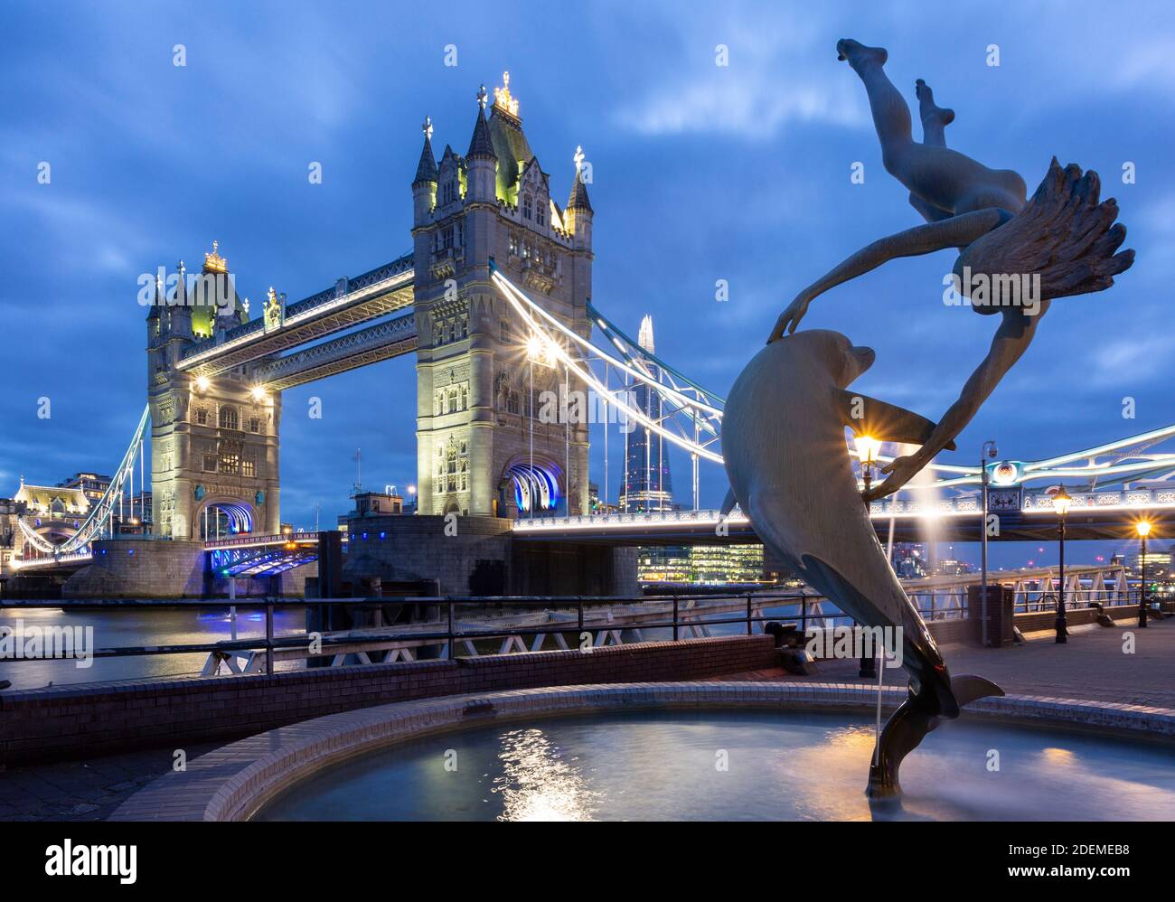 Girl with a Dolphin Fountain sculpture and Tower Bridge in background, London, March 2020 Stock Photo