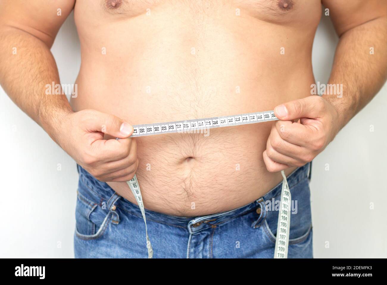 Fat man with big stomach wering jeans holding his measuring tape Stock Photo