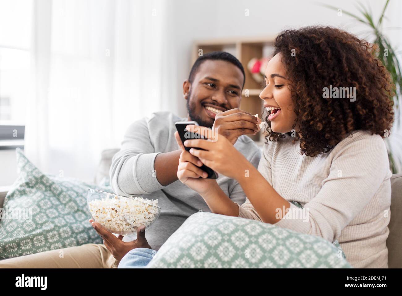 african couple with popcorn and smartphone at home Stock Photo - Alamy