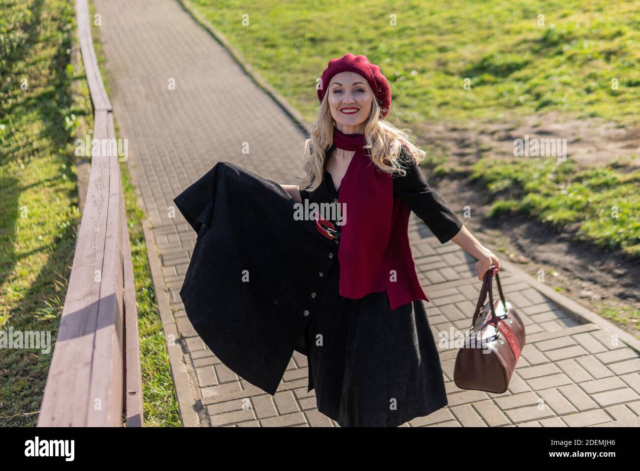 A happy lady is walking up the stairs and wearing a burgundy palette and biret, an adult is smiling at the camera in black clothes, in the fall agains Stock Photo
