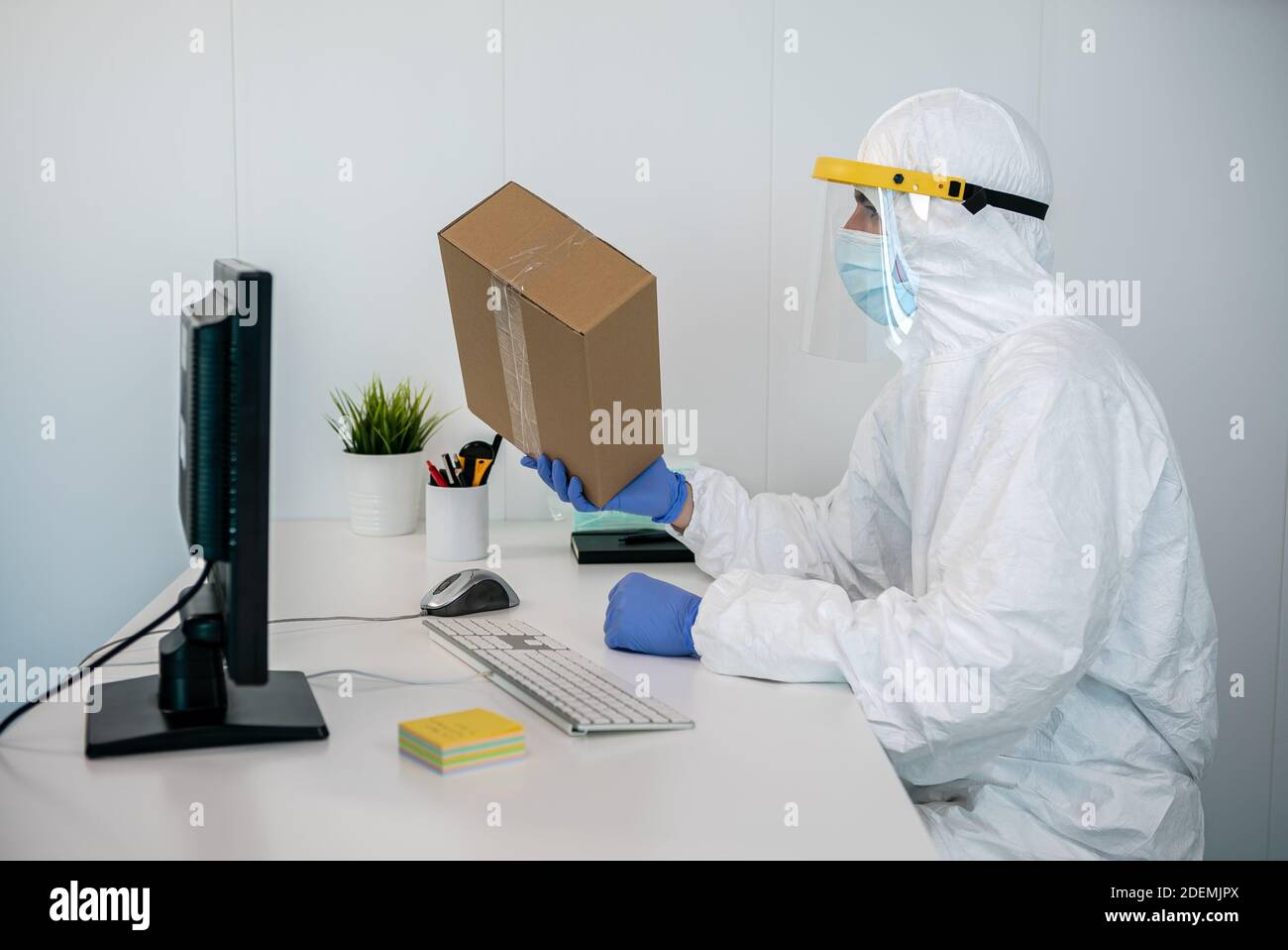 A nurse wears PPE and plastic face shield, using the computer to send ...