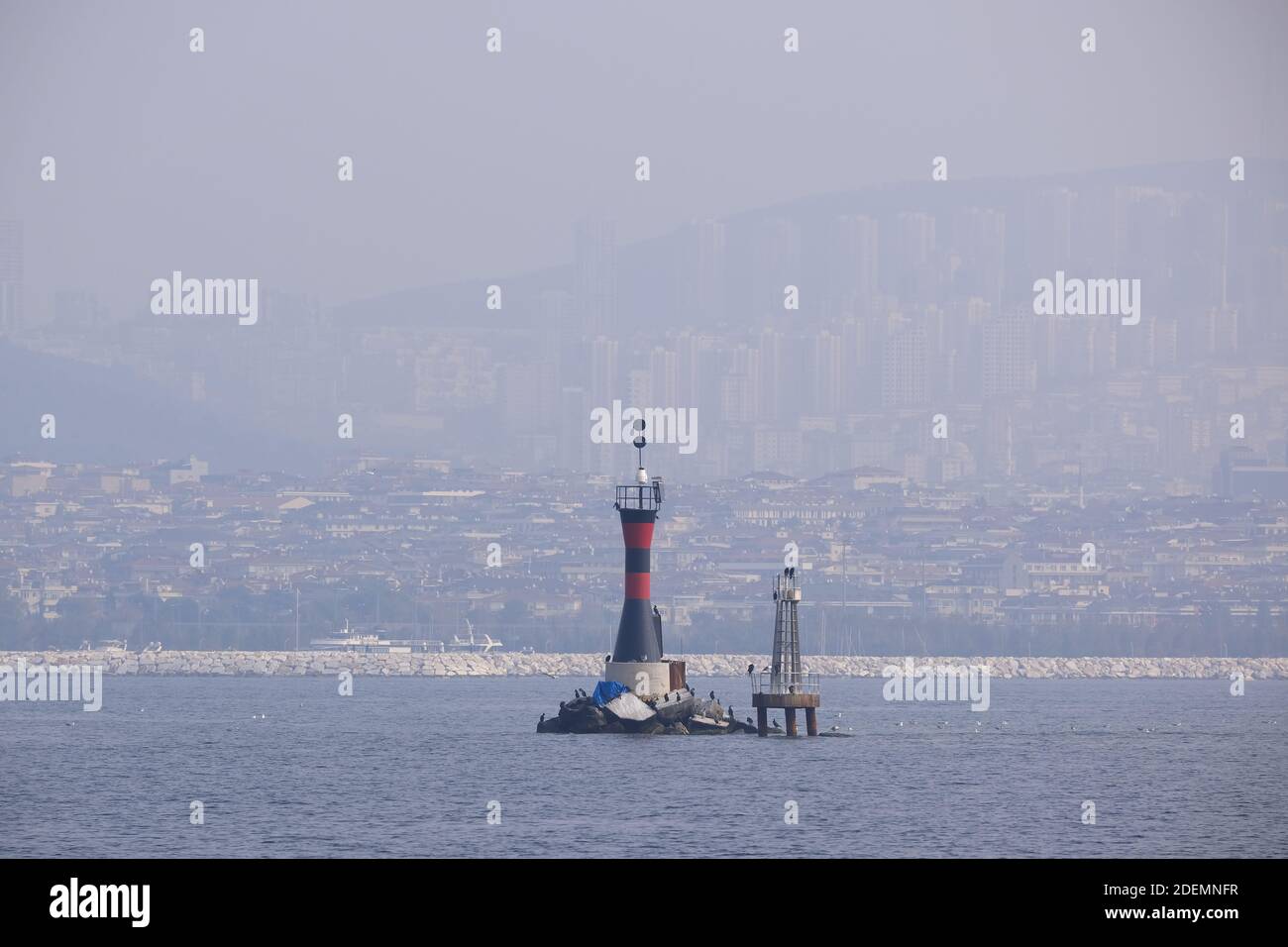 A marine rocky warning light, cityscape and seabirds in a foggy day. This little lighthouse is close to coast at Istanbul, Kartal. Stock Photo