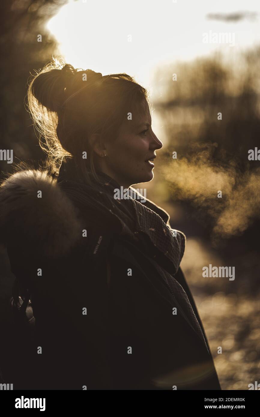 MUNICH, GERMANY - Nov 22, 2020: The silhouette of a young woman breathing cold winter air. Profile shot of the lady in the golden sunset. Stock Photo