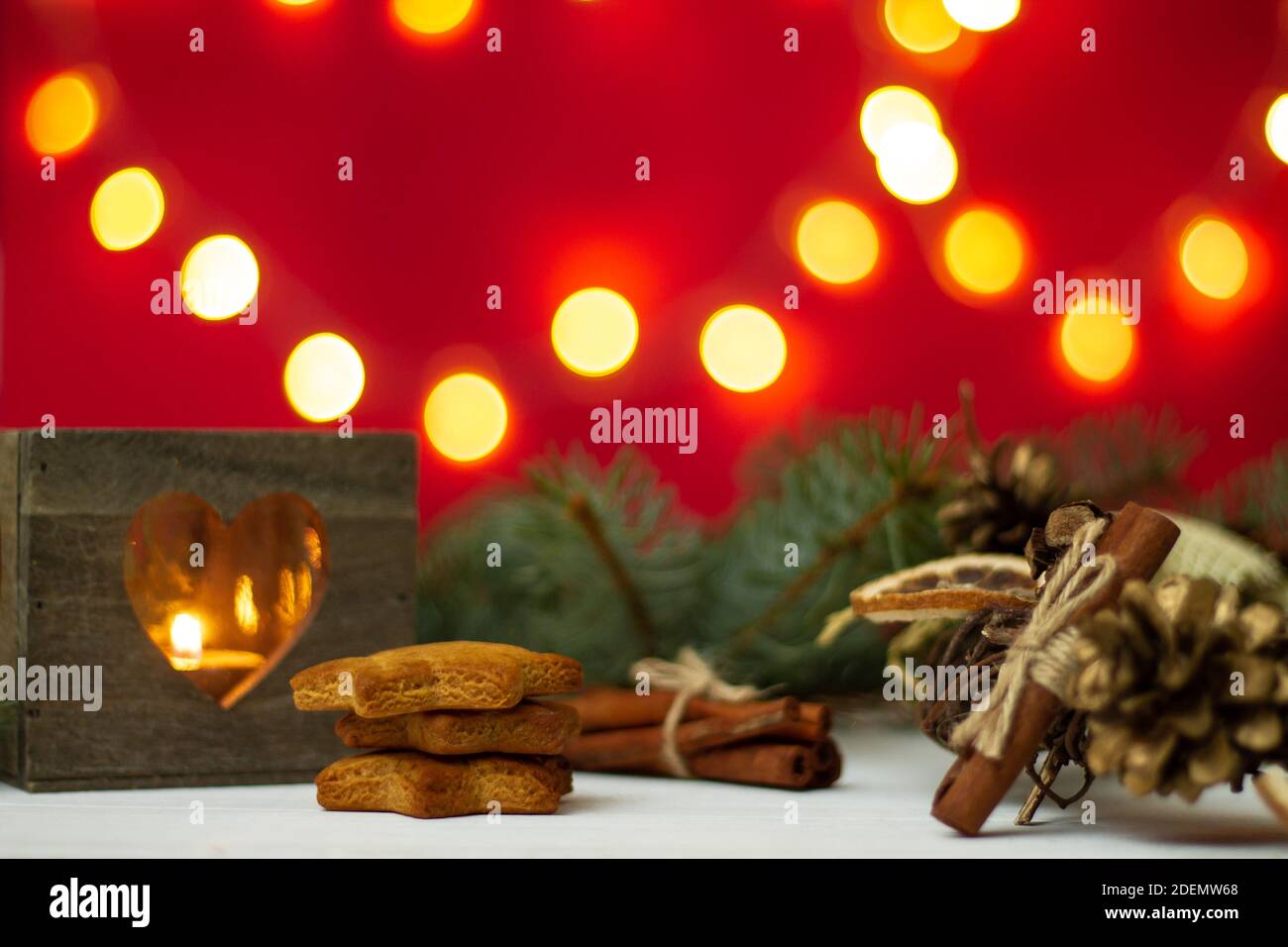 Wooden candlestick, gingerbread with Christmas tree branches and bokeh on a red background. Stock Photo
