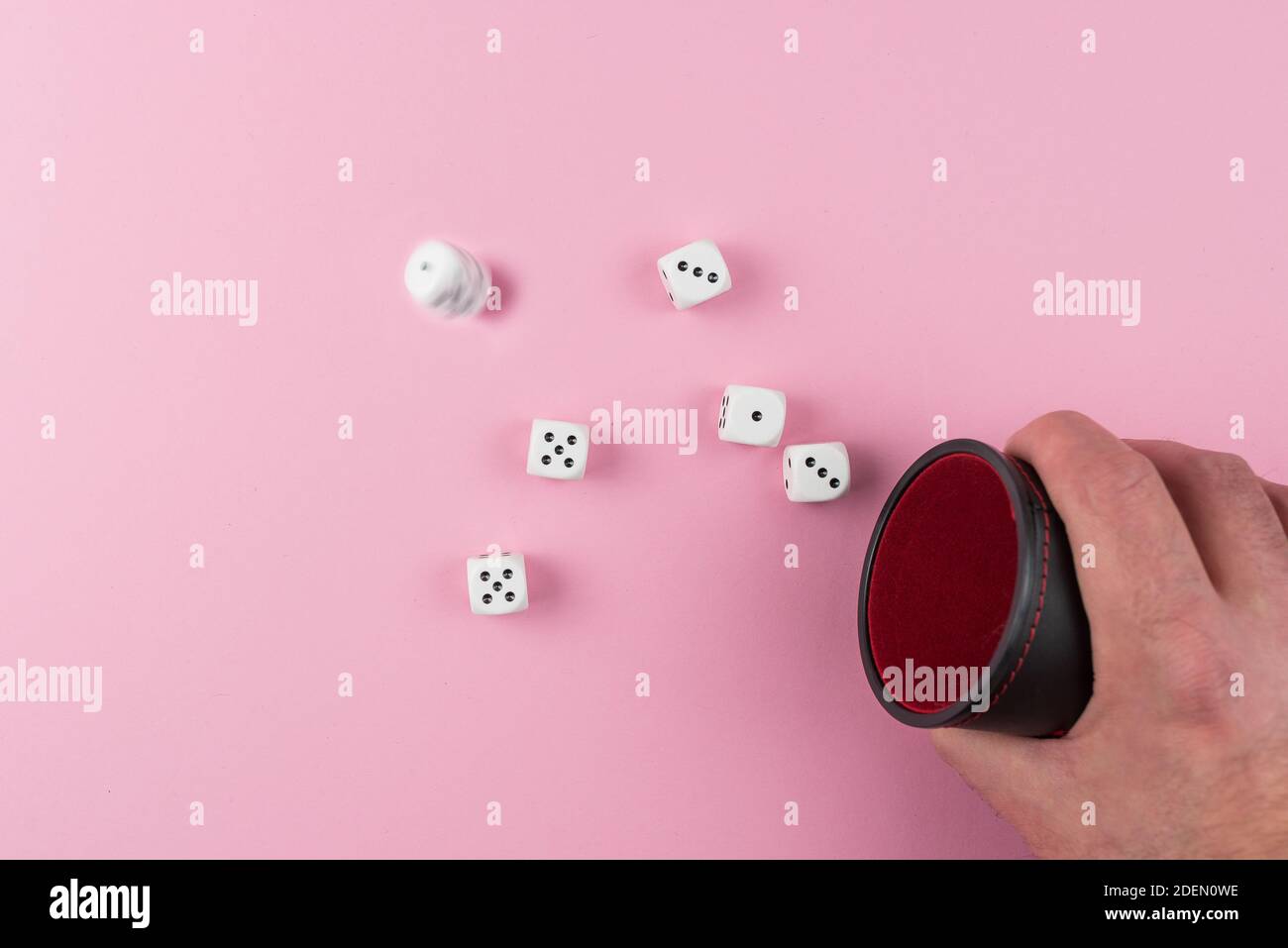 directly above view of player throwing or rolling dice using a dice shaker against pink background Stock Photo