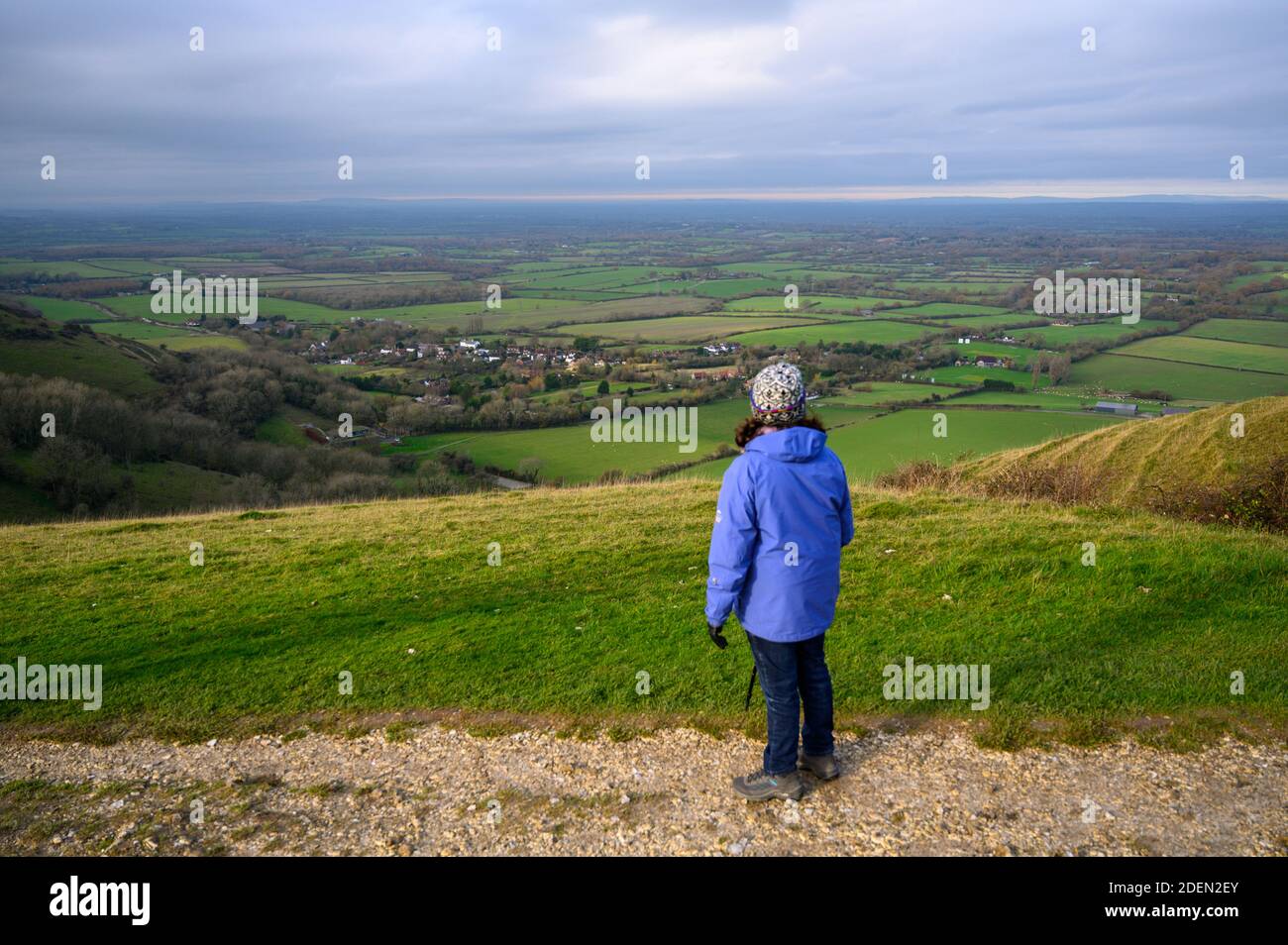 A walker on the South Downs Way in the Devil's Dyke area, West Sussex, takes in the views over Fulking village and farmland north towards North Downs. Stock Photo