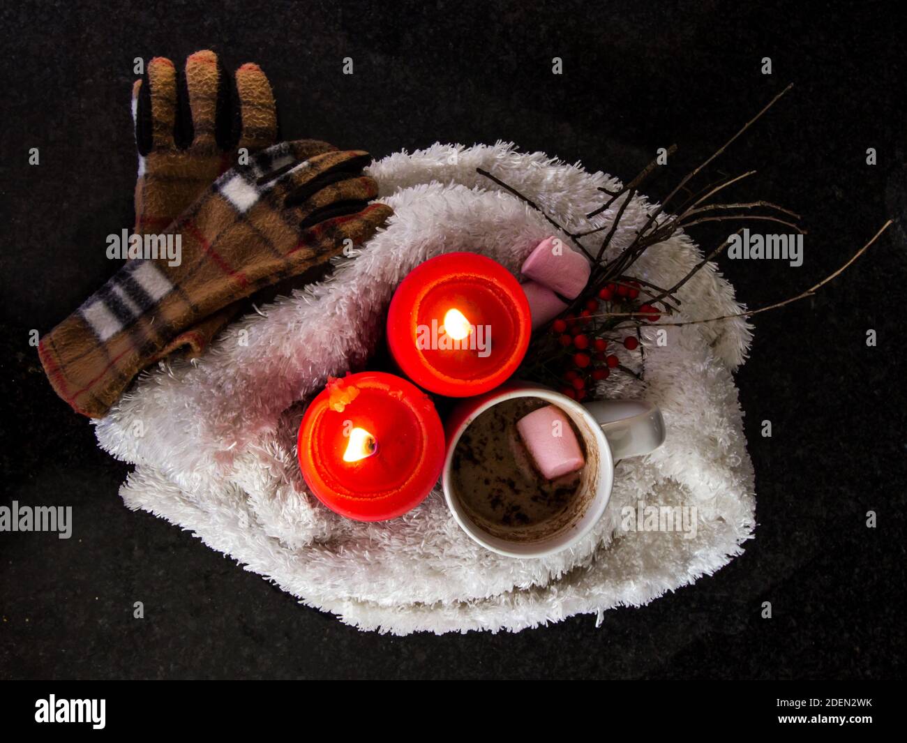 A white, red and pink winter inspired still life consisting of a scarf, gloves, candles and cocoa Stock Photo