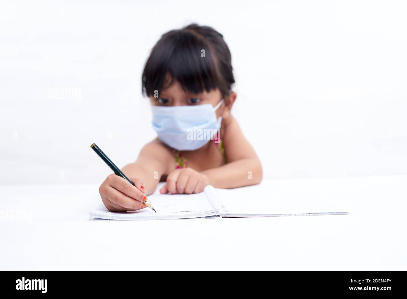 Close-up little girl hand writing in notebook, Wearing a protective face mask Stock Photo