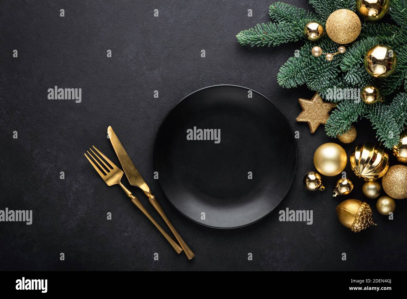 Christmas flat lay background with empty black plate, golden cutlery, christmas tree and toys. Top view, copy space. Trendy fashionable black theme Ch Stock Photo