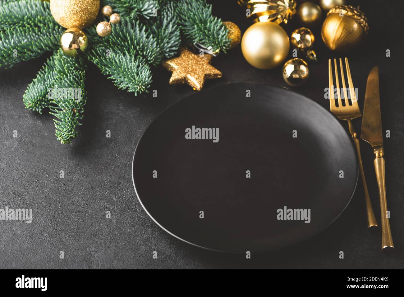 Elegant Christmas, New Year table setting in black. Black plate, golden color silverware, fir tree and toys. Copy space for text, design Stock Photo