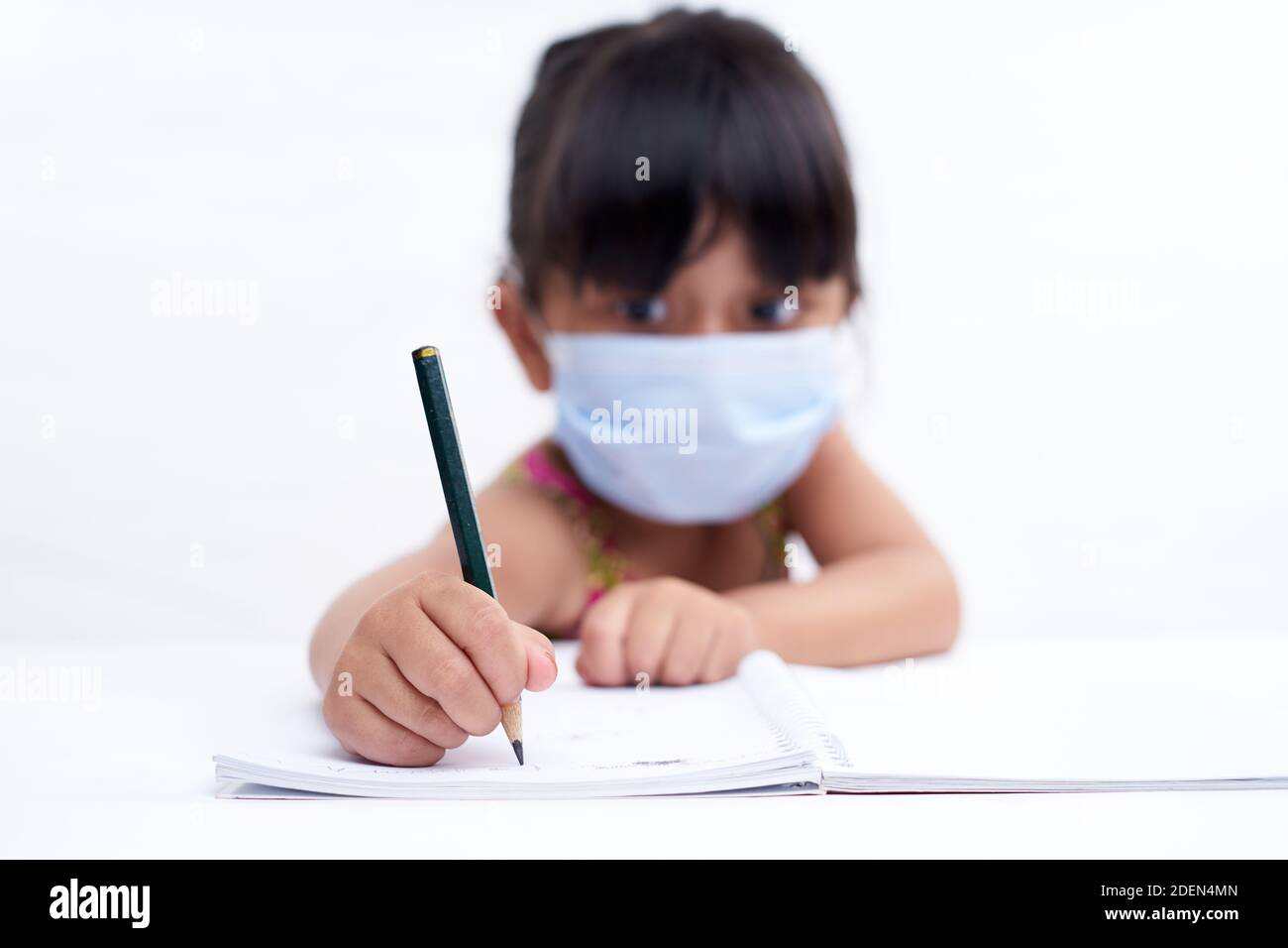 Close-up little girl hand writing in notebook, Wearing a protective face mask Stock Photo