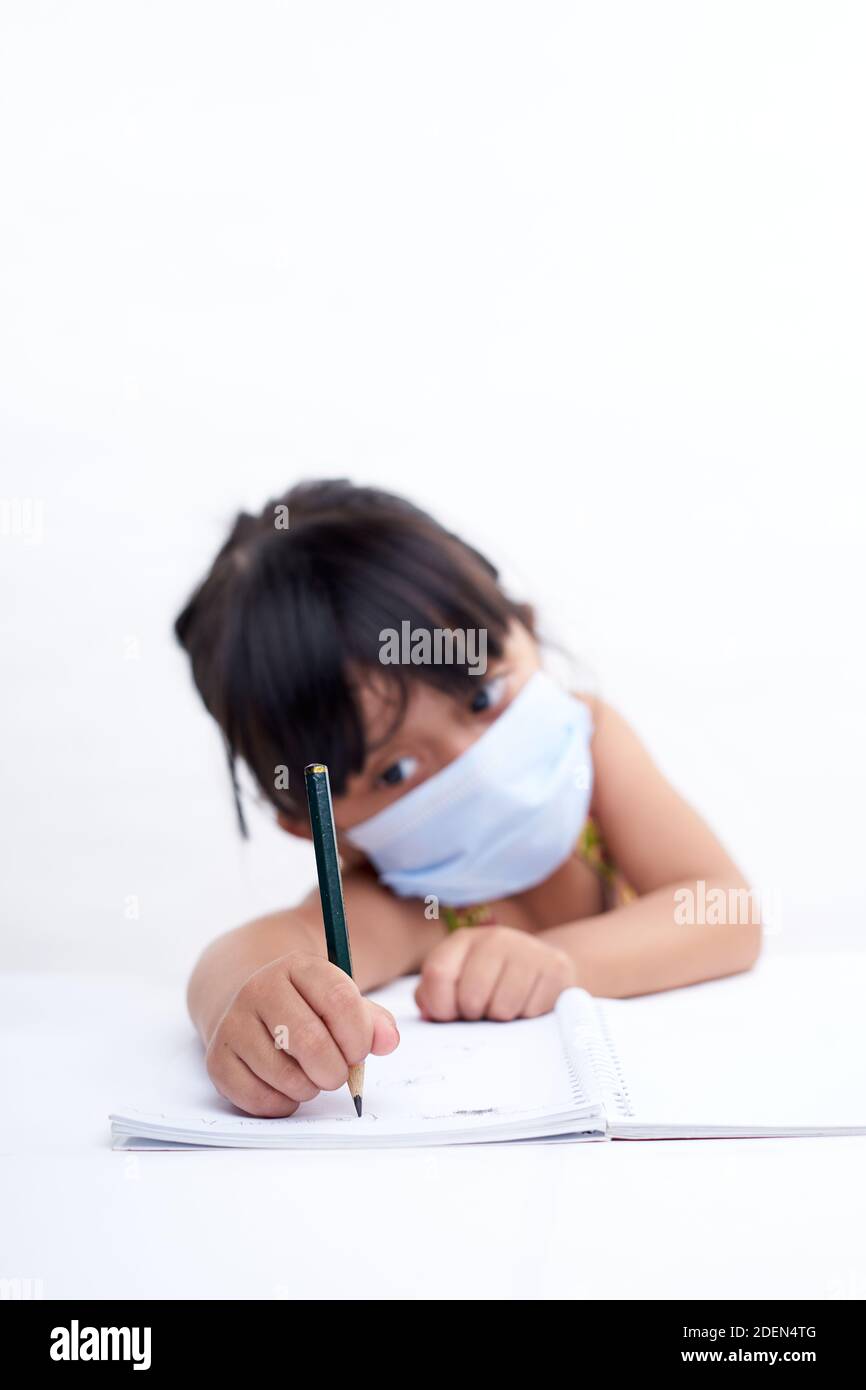 Close-up little girl hand writing in notebook, Wearing a protective face mask Stock Photo