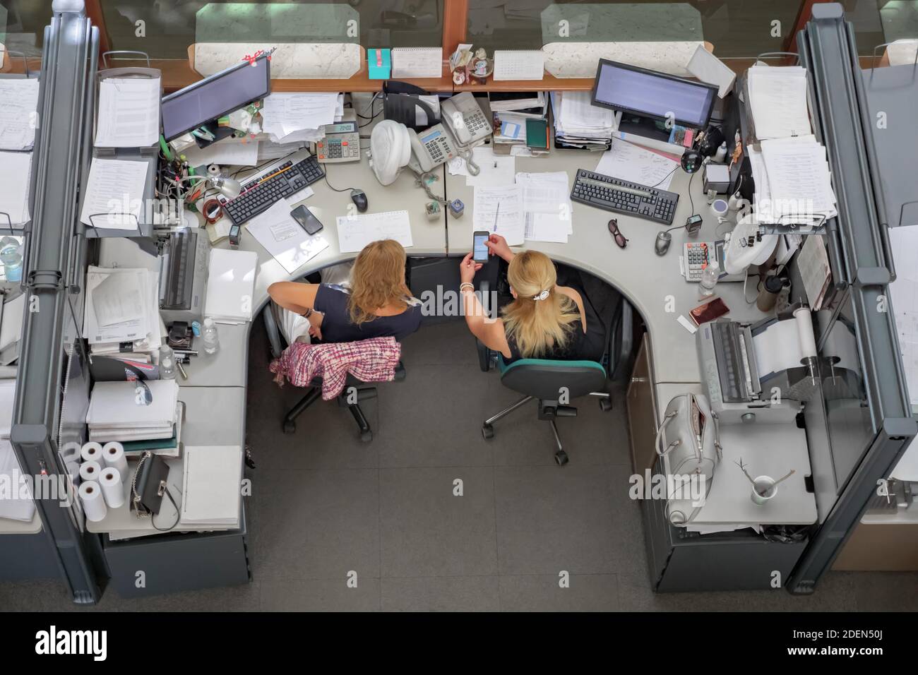 Top view. Workplace communication. Female demonstrate phone. Working days of office workers. Message on cell. Two woman, colleagues using smartphone Stock Photo