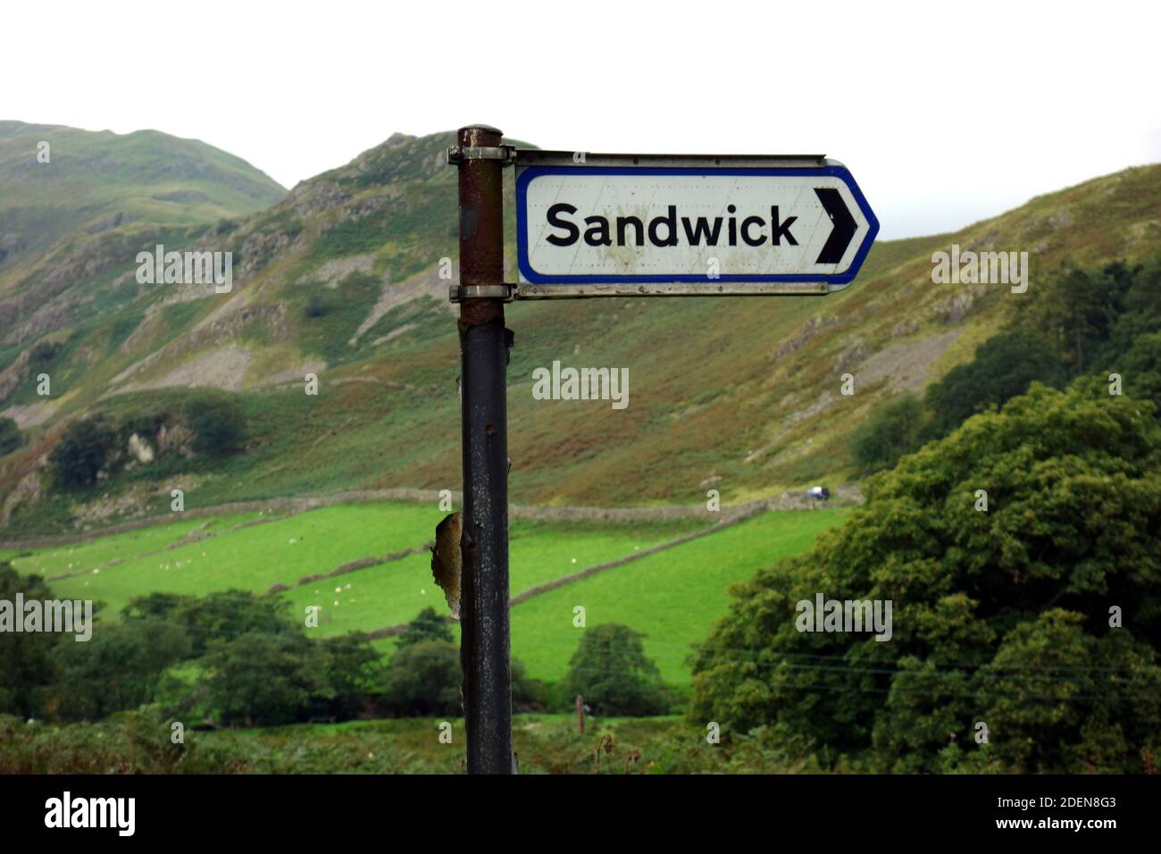 The Wainwright 'Beda Fell' & Metal Road Sign for the Hamlet of Sandwick on a Single Track Road in Martindale, Lake District National Park, Cumbria. Stock Photo