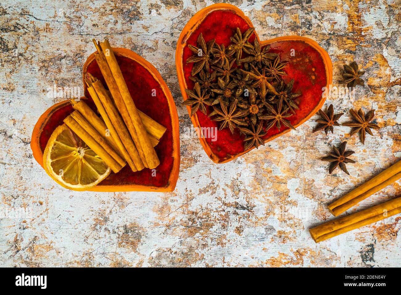 Cinnamon sticks, star anise and dried citrus in red bowls with a heart shape on a light grunge background. Winter spices used with mulled wine. Stock Photo