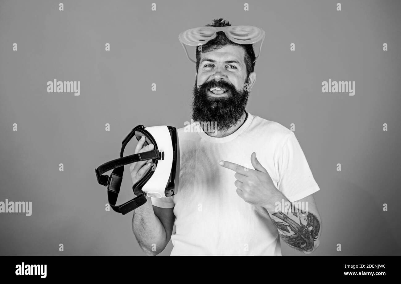 Man bearded hipster with virtual reality headset and louvered sunglasses red background. Alternative reality. Which glasses choose louvered or virtual. Man making decision what choose real or virtual. Stock Photo