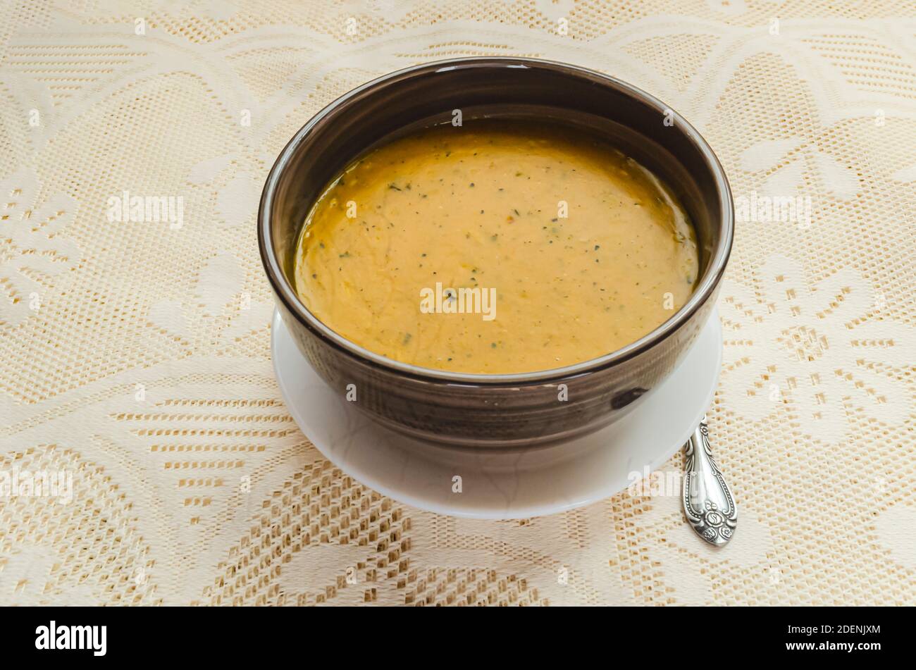 On a lacey background is a brown striped bowl of rich thick meatless pumpkin soup. Stock Photo