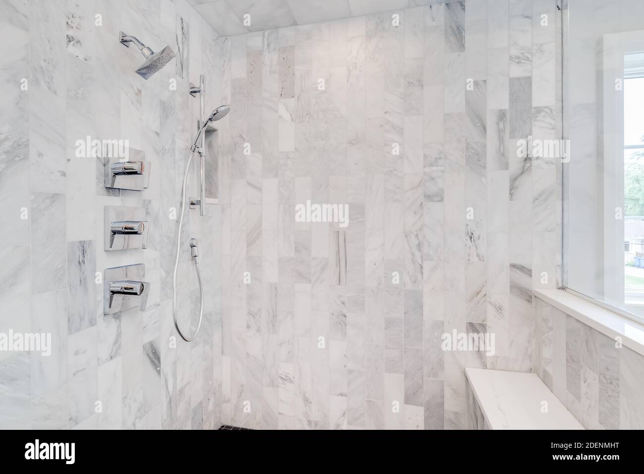 The interior of a gorgeous marble tiled shower with chrome faucet and a seat. Stock Photo