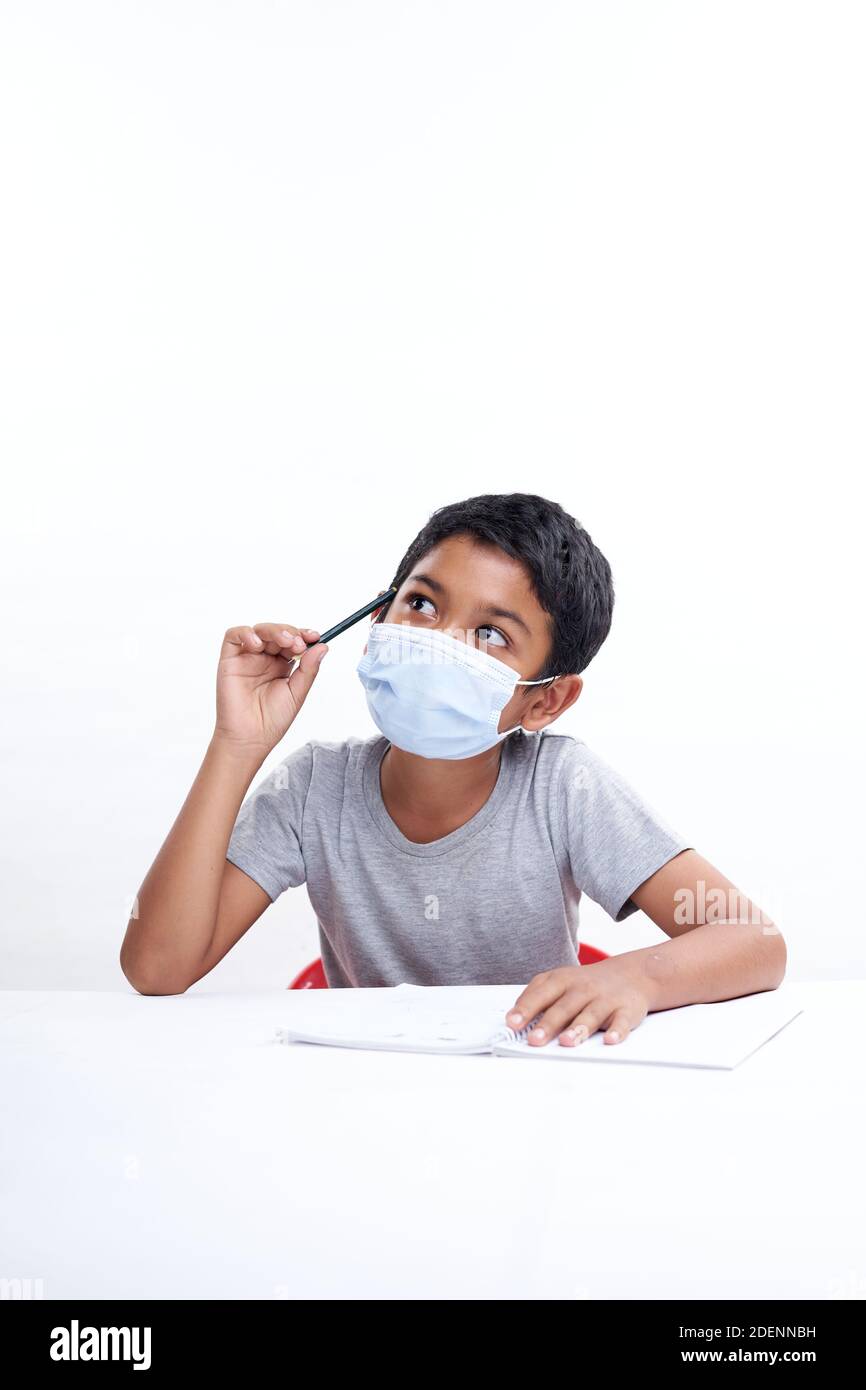 Schoolboy with a protective face mask writing in notebook at home, Homeschooling New Normal education concept Stock Photo