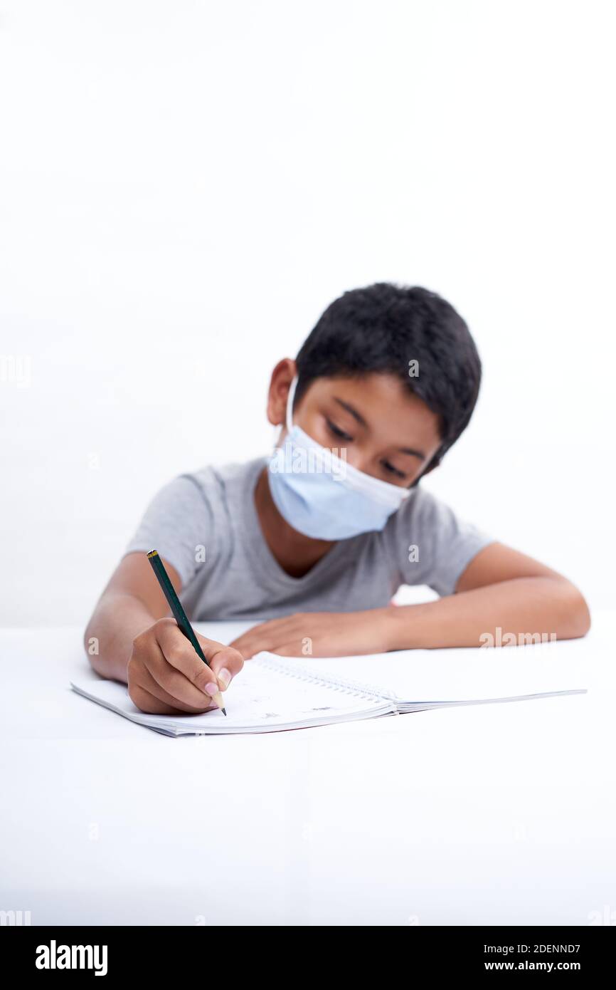 Schoolboy with a protective face mask writing in notebook at home, Homeschooling New Normal education concept Stock Photo