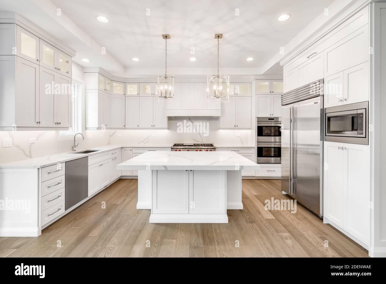 A luxurious modern white kitchen with stainless steel Wolf, Subzero, and Whirlpool appliances. Stock Photo