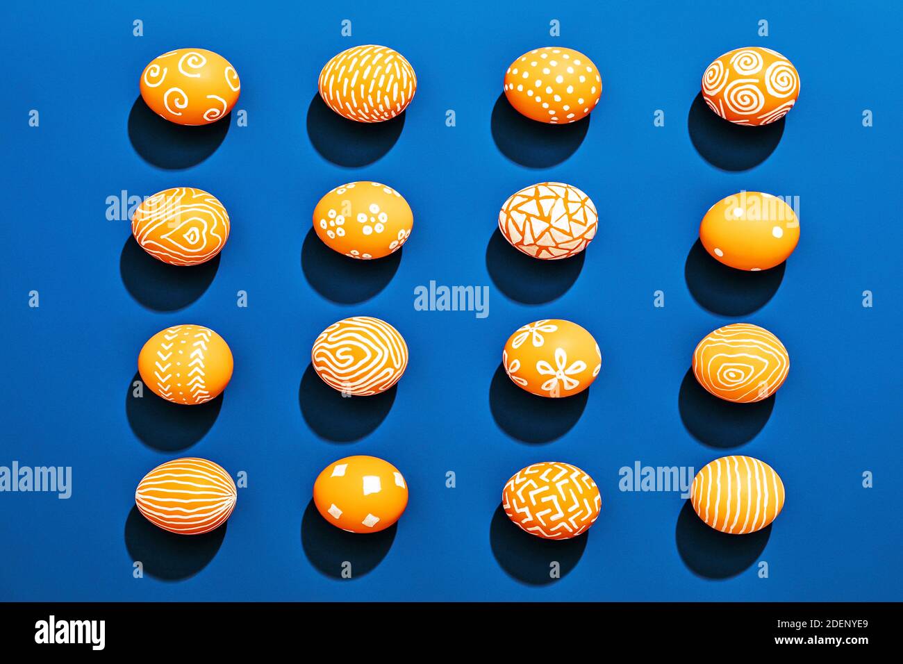 Orange colored Easter eggs pattern on contrasting blue background Stock Photo