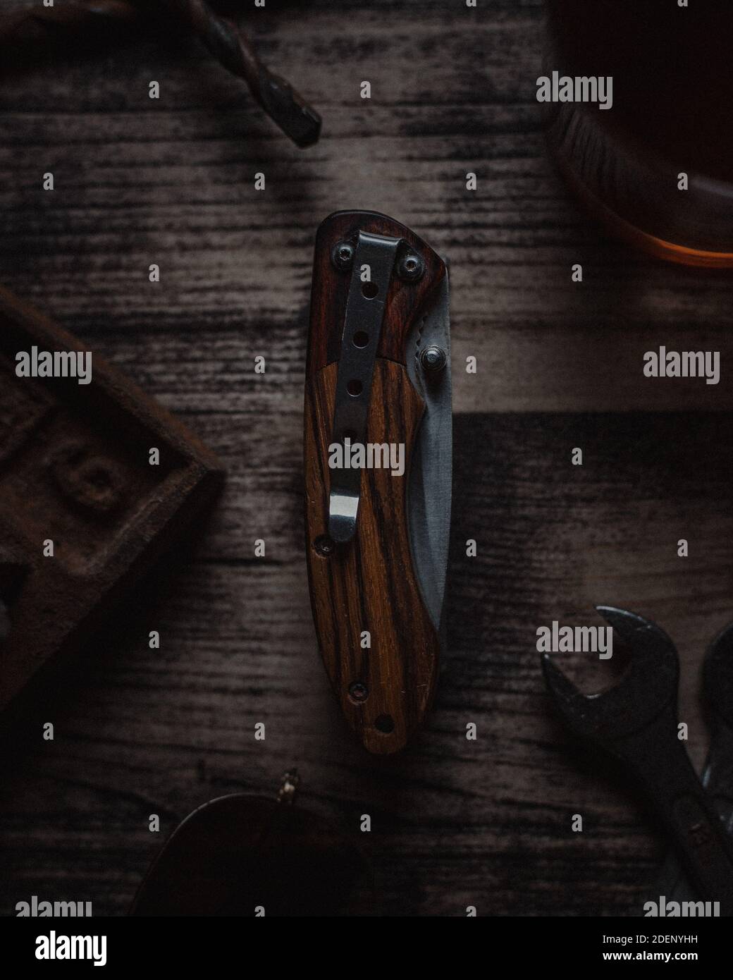 Folded knife displayed on a wooden table surrounded by various work tools Stock Photo