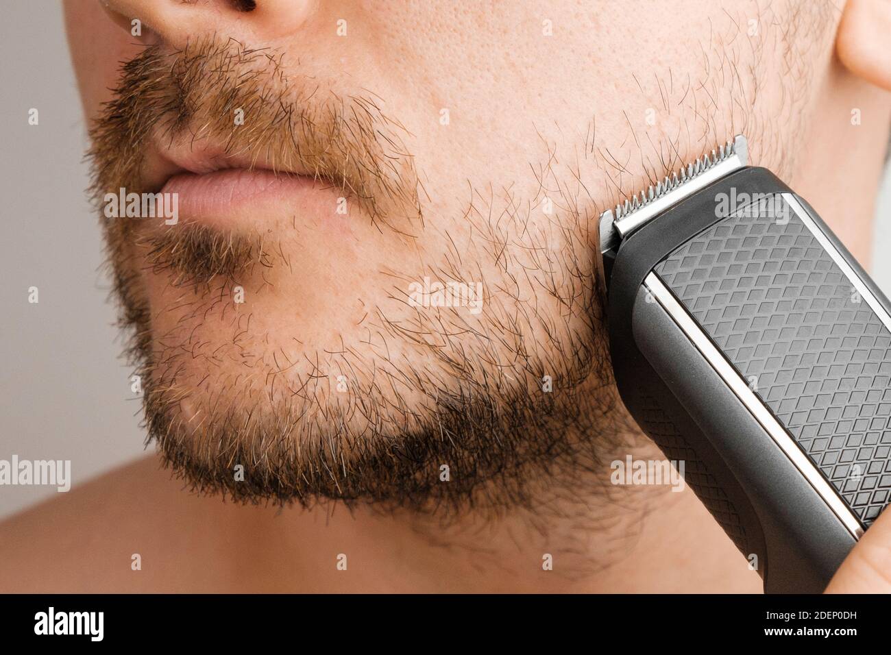 Man shaving beard and cheeks with an electric razor. Morning routine