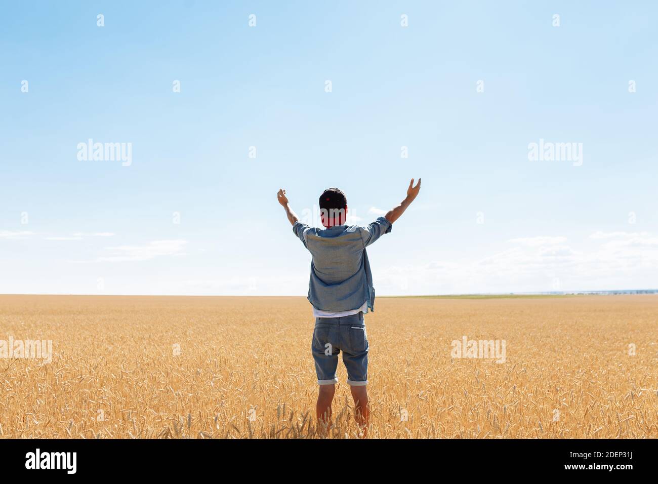 the man raised his hands to the sky, against the background of a wheat field, the guy in the cap and shirt Stock Photo